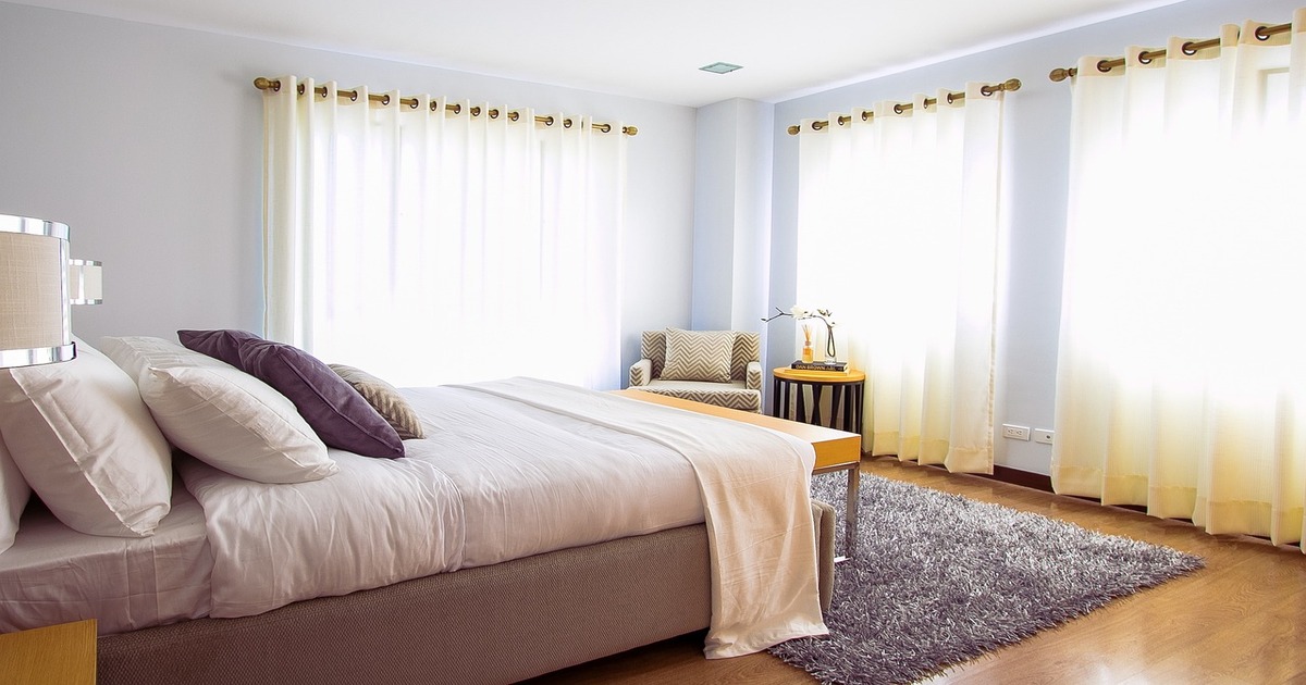 A sunny and airy bedroom containing a bed with white bedding.