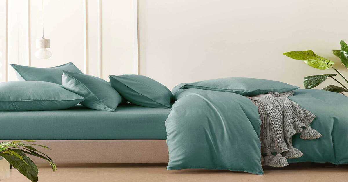 A bed with duck-egg bamboo bed sheets and pillowcases in a well-lit room.