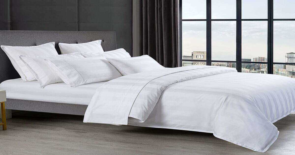 A bed lined with white stripped Egyptian cotton bed sheets. 