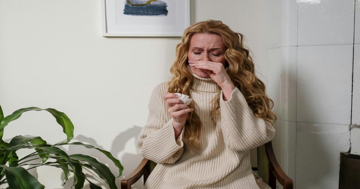 A woman sneezing, wondering about the best sheets for allergies to help her.